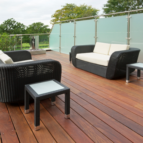 Deck with various shades of brown composite decking, black and cream patio furniture, and opaque glass railing surrounding the area.